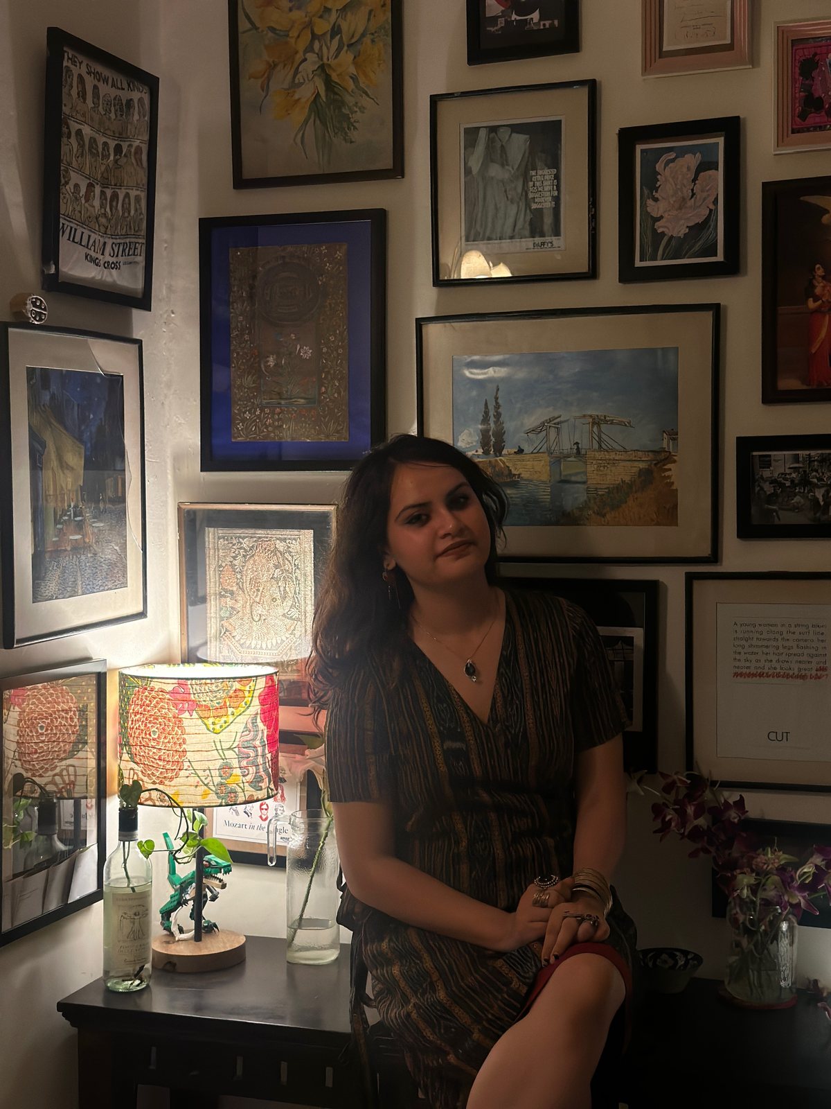 Shrija Jha — seated before a gallery wall of paintings and prints